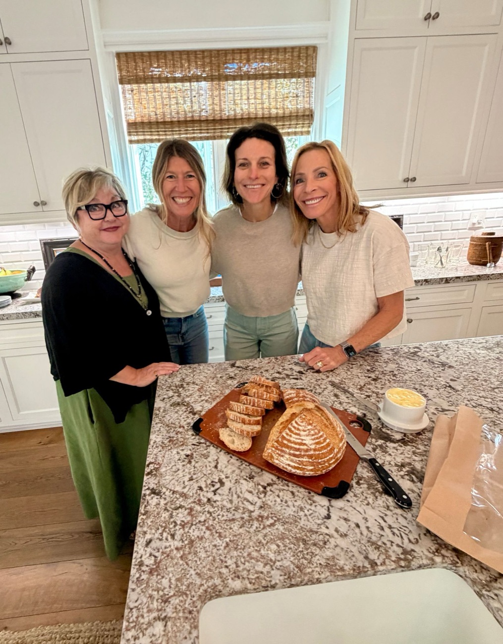Four women smiling around a kitchen island with fresh bread